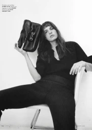 Model seated on a white chair holding a black leather handbag, photographed in monochrome for iO Donna.