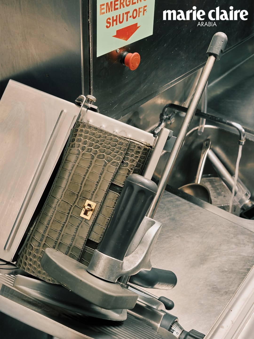 Marie Claire Arabia fashion shot: Leather purse on a slicer against a metallic background with an emergency shut-off switch.
