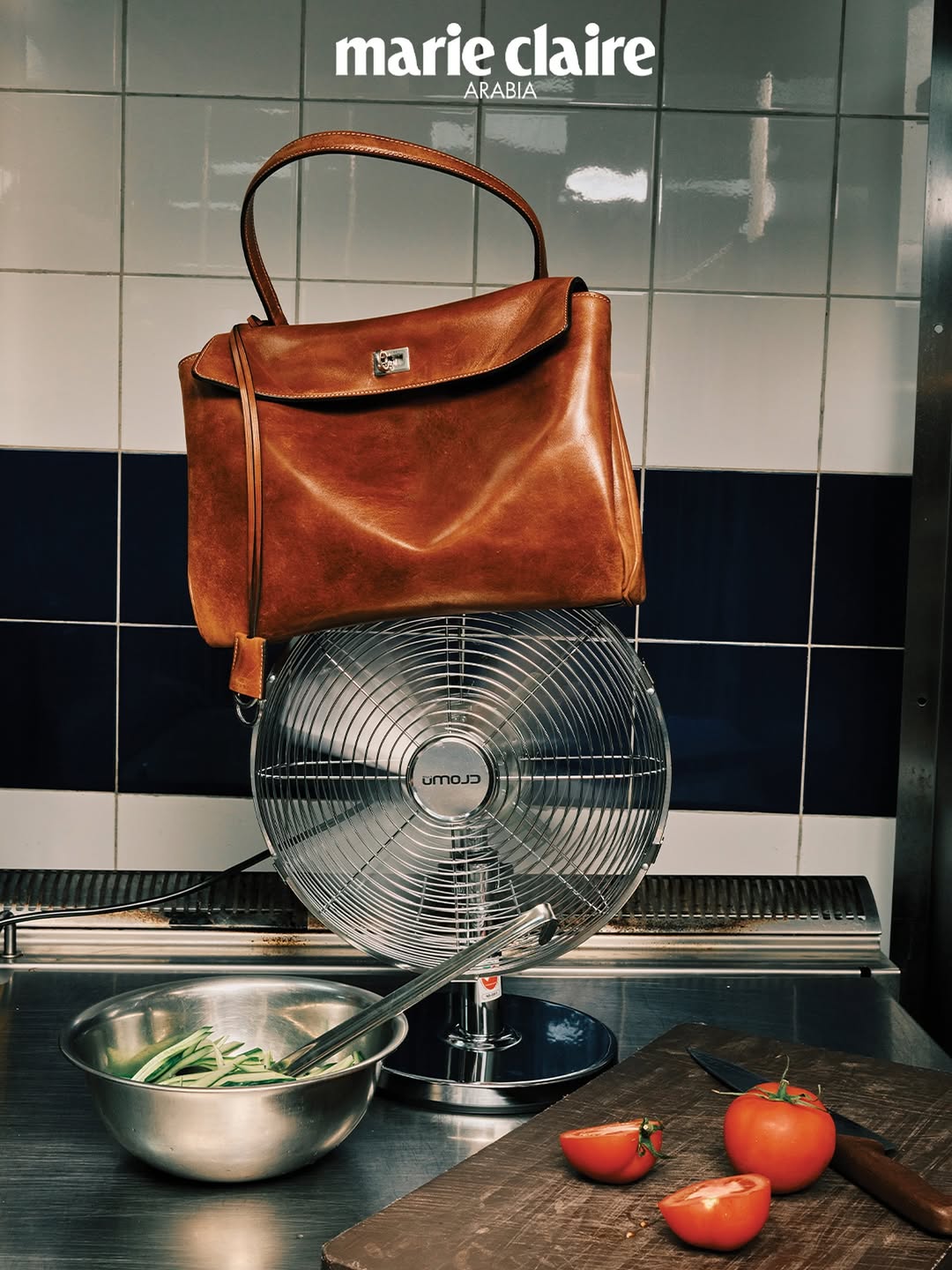 Brown leather handbag on a silver vintage fan with food ingredients next to a tiled wall, shot for Marie Claire Arabia.