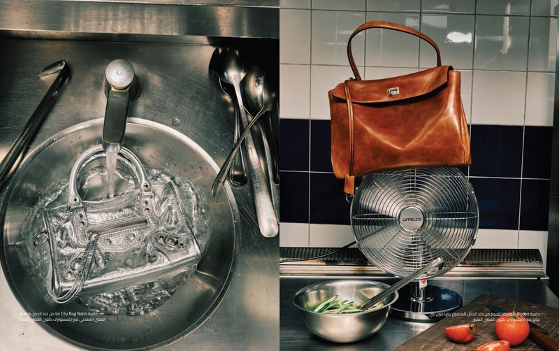 Two handbags are presented in a conceptual manner, one being washed in a stainless steel sink and the other sitting on a vintage fan.