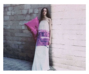 Model standing against a stone wall holding a pink pillow in a fashion editorial for W Magazine.