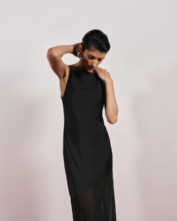 Model in a black slip dress with sheer hem posing against a plain light background for Cue Spring 24