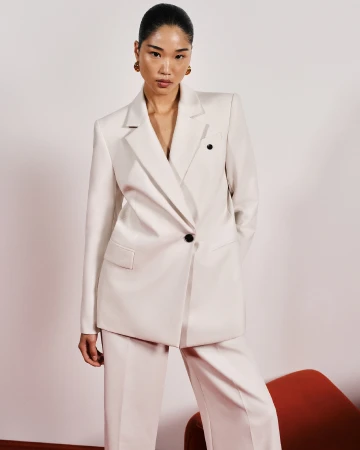 Asian woman wearing a cream oversized blazer and matching trousers against a pale background for Cue Spring 24.