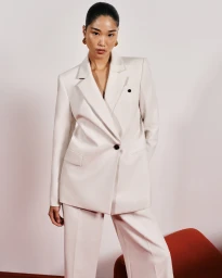Asian woman wearing a cream oversized blazer and matching trousers against a pale background for Cue Spring 24.