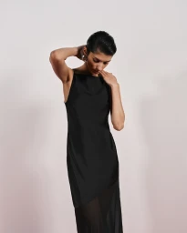 Model in a black slip dress with sheer hem posing against a plain light background for Cue Spring 24