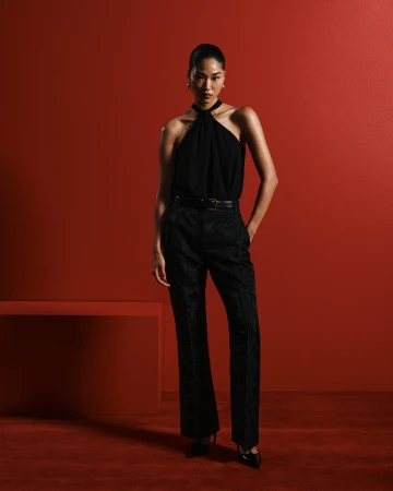 Model in a black halter top and trousers posing against a deep red studio backdrop for Cue Spring 24 campaign
