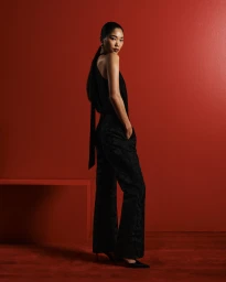 Model in black sleeveless top and patterned trousers standing against a vibrant red studio background for Cue Spring 24