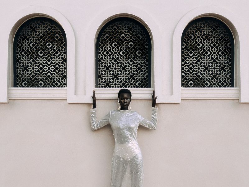 Elegant black female fashion model in shimmering gown posing by arched Moorish windows. Beauty and high fashion photography.