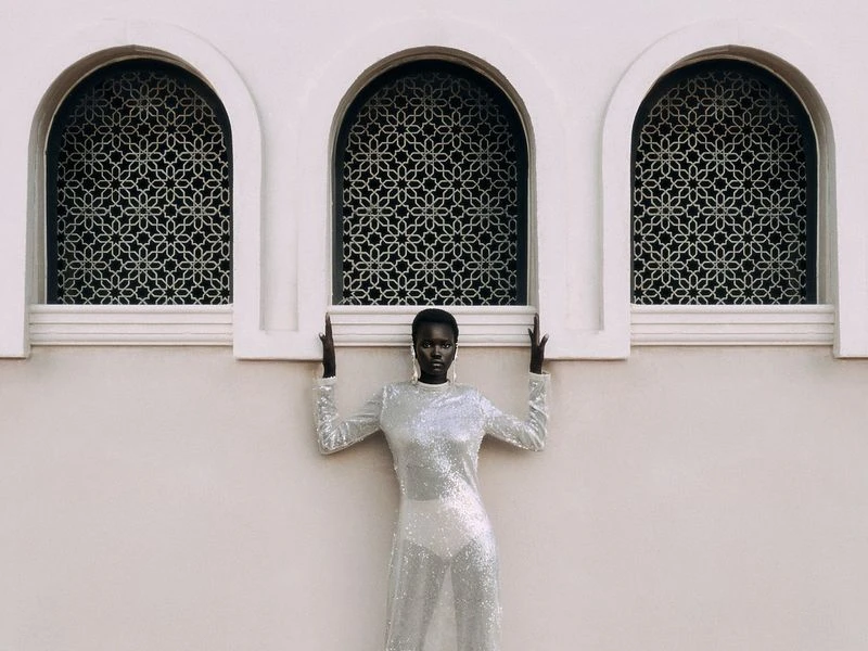 Elegant black female fashion model in shimmering gown posing by arched Moorish windows. Beauty and high fashion photography.