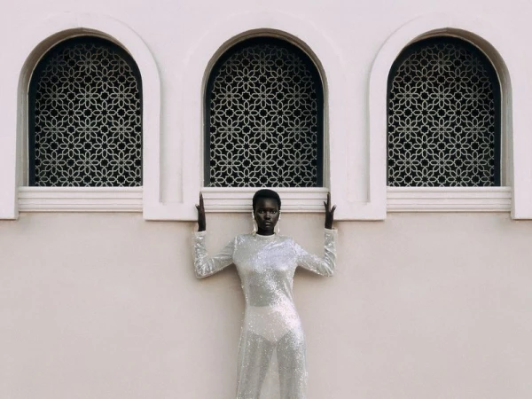Elegant black female fashion model in shimmering gown posing by arched Moorish windows. Beauty and high fashion photography.