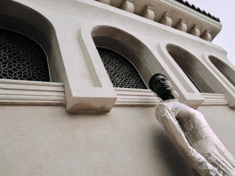 Black woman in a textured white dress posing against an ornate light-colored building exterior with arched windows