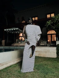 Model in a black and white striped cut-out gown standing outdoors near a lighted pool at night for an editorial project.