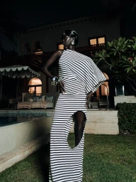 Model in a black and white striped cut-out gown posing on a lawn at night in front of a luxury resort poolside.