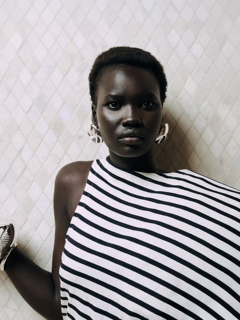 Black woman wearing a striped top and large silver earrings against a pale patterned tile wall