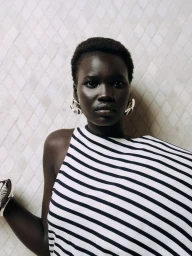 Black woman wearing a striped top and large silver earrings against a pale patterned tile wall