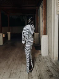 Black woman wearing a black and white striped dress standing in an open hallway with wooden columns
