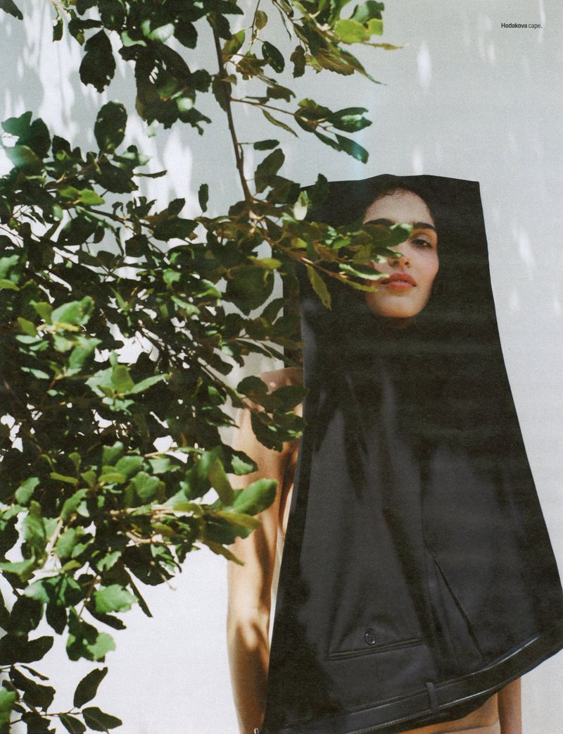 Model Sara Caballero draped in black tailored trousers next to tree foliage against a sunlit white wall for W Magazine.