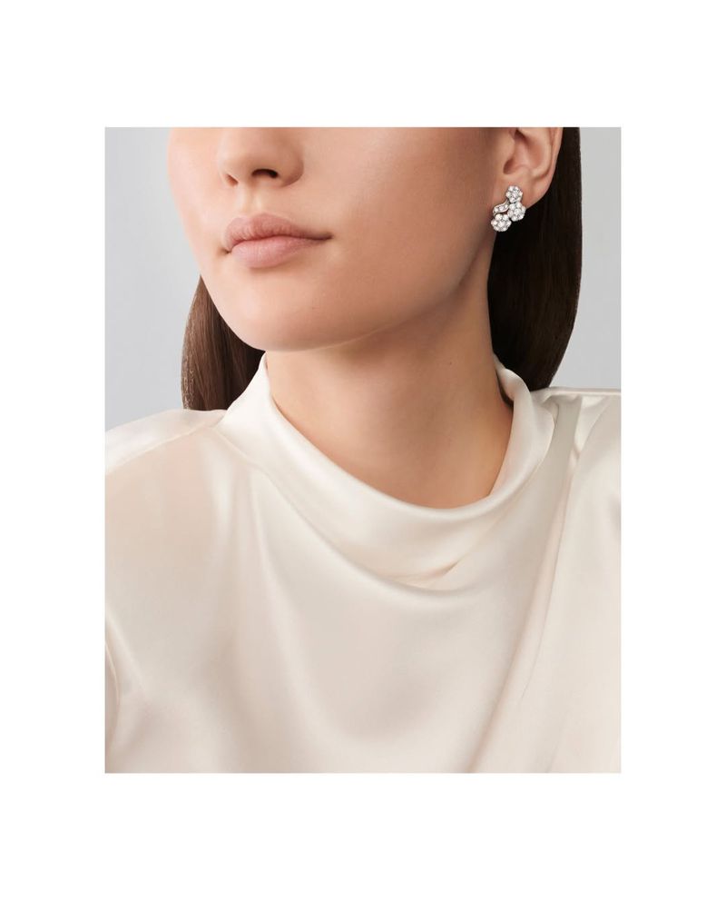 Close-up of a fair-skinned woman with an updo hairstyle, wearing floral diamond earrings and a white, cowl-neck blouse.