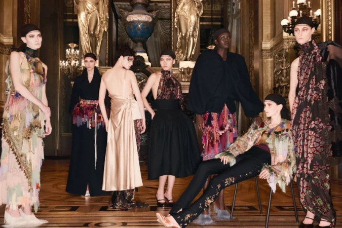 A group of seven fashion models in a grand hall displaying an assortment of dresses and separates with muted tones and elegant details.