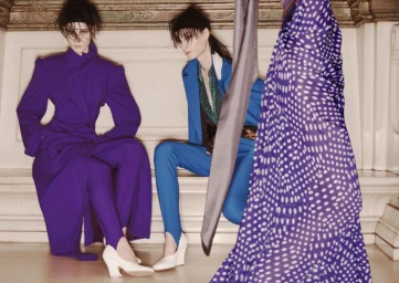 Two models in vibrant purple and blue tailored suits seated against a classical stone interior