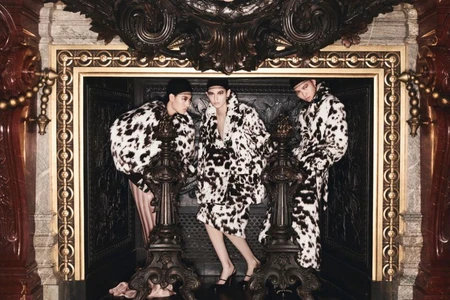 Three models wearing dalmatian print coats posing inside an ornate stone fireplace mantel