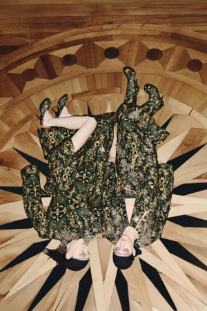 Two models lying on a geometric wooden parquet floor wearing patterned green garments for Dries Van Noten Fall/Winter 2025