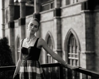 Model Anna Palgen wearing a dark strapless dress with a patterned skirt outdoors against a historic stone building facade.