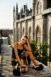 Model seated on a wooden rooftop terrace wearing a black top and plaid skirt against a historic stone building.