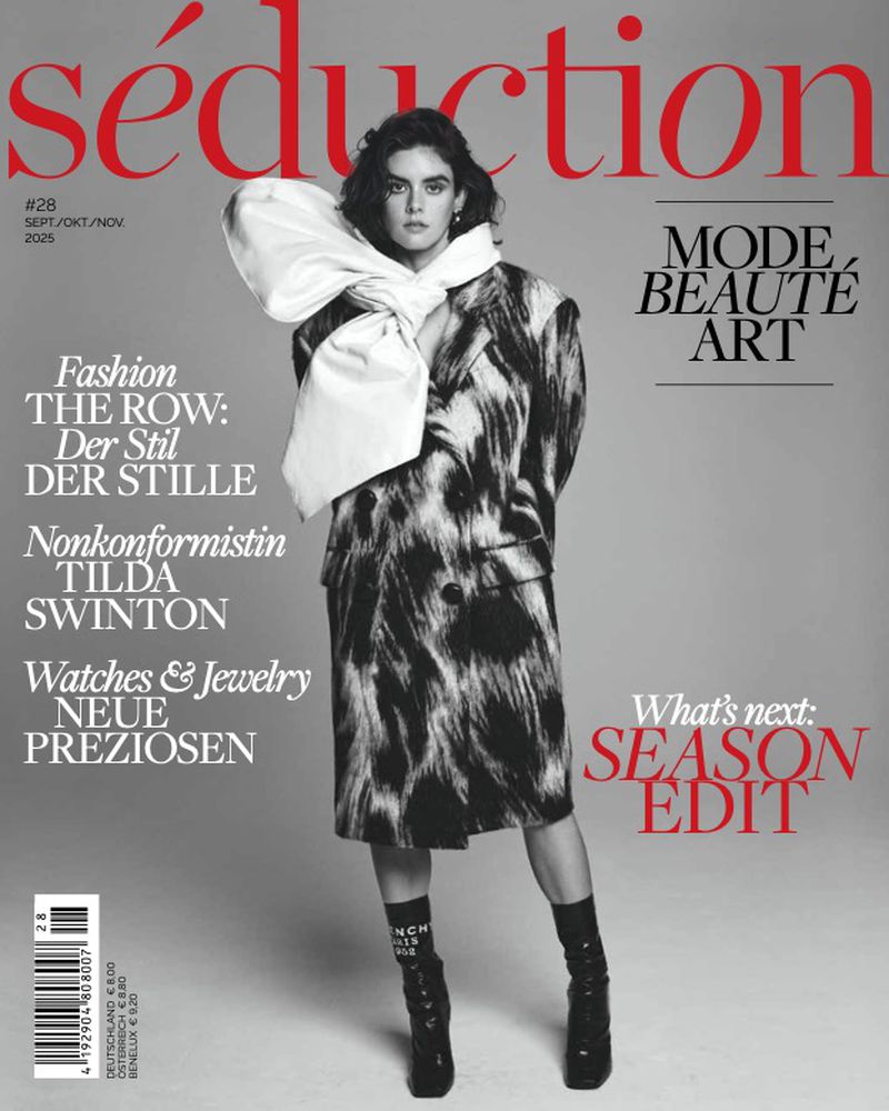 Magazine cover featuring a female model in a patterned coat with a large white bow, black socks, and heeled boots, against a grey background.
