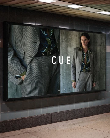 Fashion advertisement featuring a woman in a gray suit, posing against a concrete wall, next to a close-up of a matching gray suit.