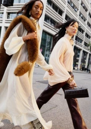 Two female models walking outdoors in front of a modern urban building exterior for an H&M campaign