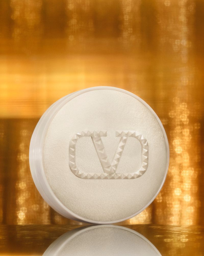 Cosmetic powder compact from Valentino Beauty with logo on a gold background. Beauty product image for makeup and skincare advertising.