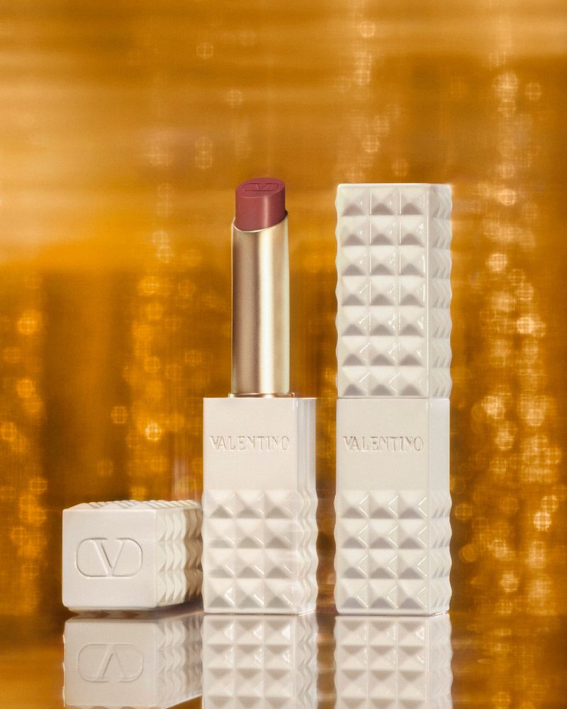 Valentino lipstick with embossed case and lid, displayed against a shimmering gold background in a beauty and fashion-forward image.