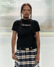 Model wearing a black t-shirt and plaid skirt standing against a ribbed glass wall for Carhartt Women's S/S 25