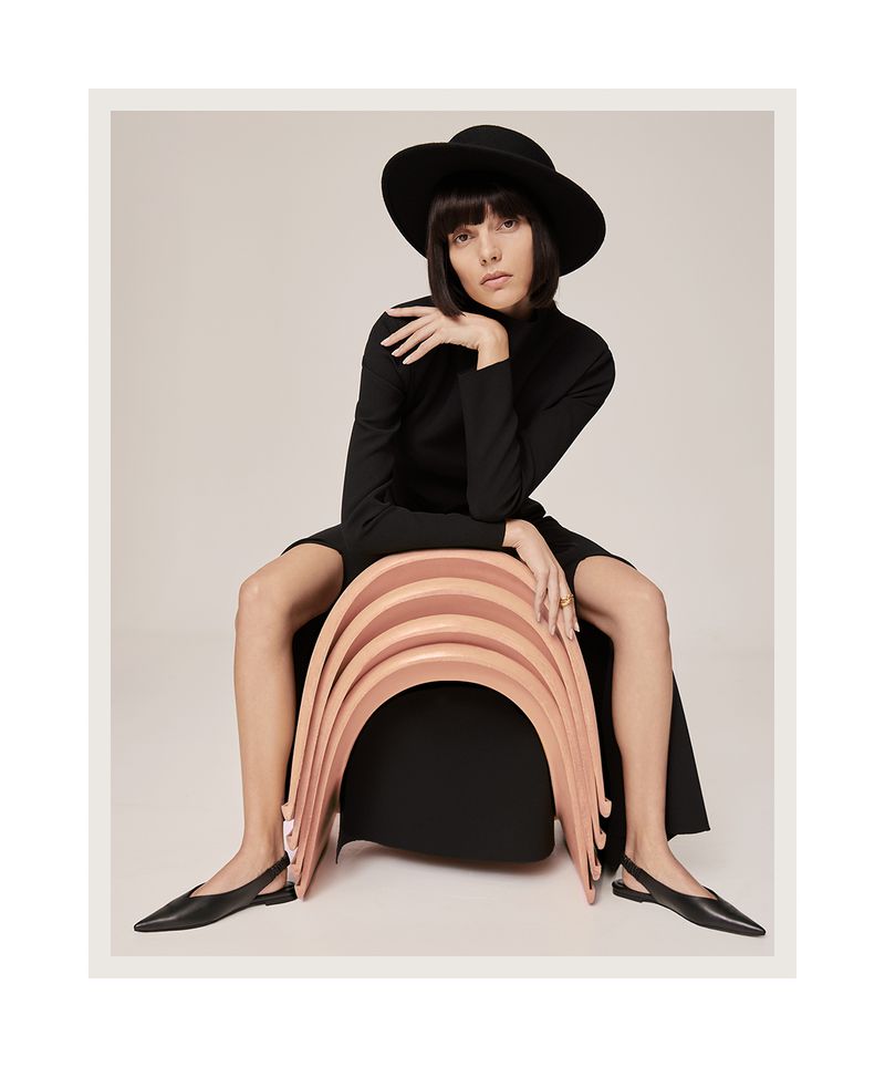 Charlee Fraser seated on a stack of curved pink chairs wearing a black dress and wide-brim hat for Harper's Bazaar Australia