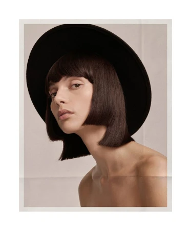Close-up portrait of model Charlee Fraser wearing a black wide-brim hat and blunt bob haircut against a white studio background.