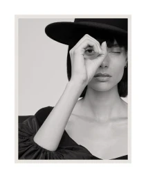 Charlee Fraser wearing a black hat, looking through hand framing eye for Harper's Bazaar Australia Issue South America.