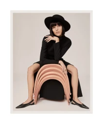 Charlee Fraser seated on a stack of curved pink chairs wearing a black dress and wide-brim hat for Harper's Bazaar Australia