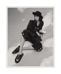 Charlee Fraser seated in a dark blazer, wide shorts, black hat and sandals against a pale sandy dune for Harper's Bazaar Australia.