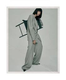 Charlee Fraser posing in a grey oversized suit holding a chair against a plain studio background for Harper's Bazaar Australia