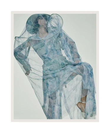 Model Charlee Fraser wearing sheer blue patterned veil and matching apparel against a light grey studio backdrop.