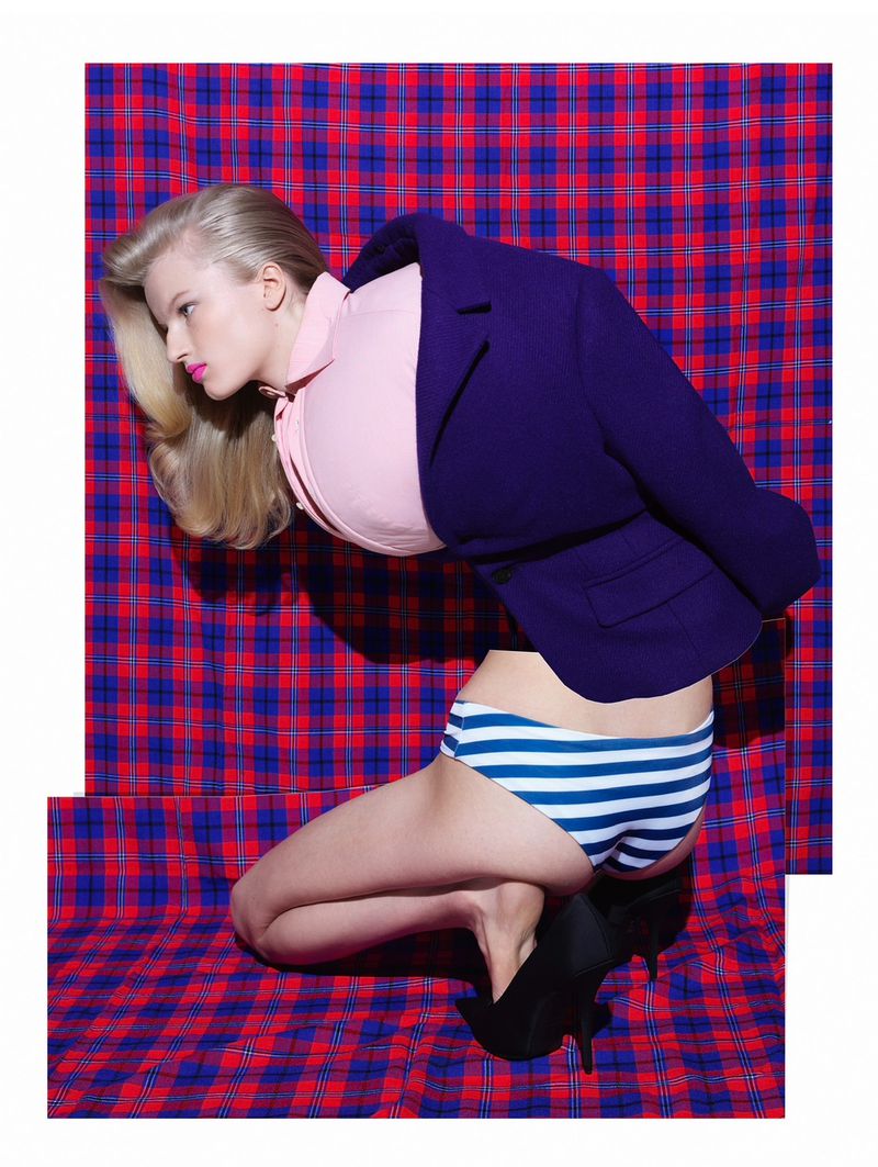 Blonde woman in blue jacket and striped underwear poses on red and blue plaid patterned background in a fashion shot.