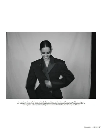 A smiling woman in a stylish black suit poses in a photo studio against a neutral backdrop, exuding confidence and modern fashion.