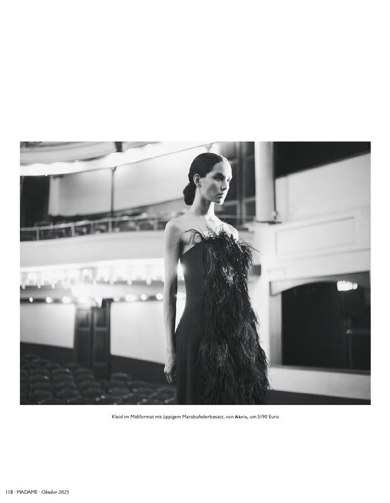 Monochrome fashion shot: Woman in elegant black strapless dress with feather detail, posing in vintage theater with empty seating.