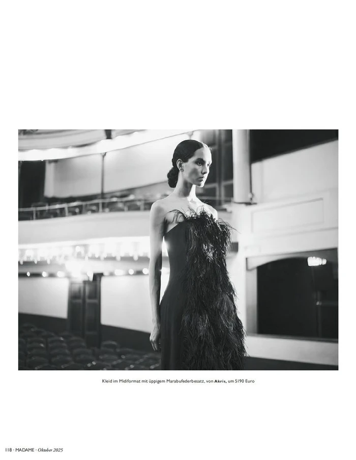 Model Eduarda Vieira in a black strapless feather-embellished gown standing inside an empty theater auditorium.