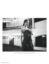 Model Eduarda Vieira in a black strapless feather-embellished gown standing inside an empty theater auditorium.