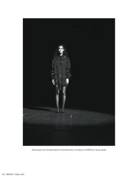 Model Eduarda Vieira wearing a dark sheer shirt dress standing in a spotlight against a pitch black background.
