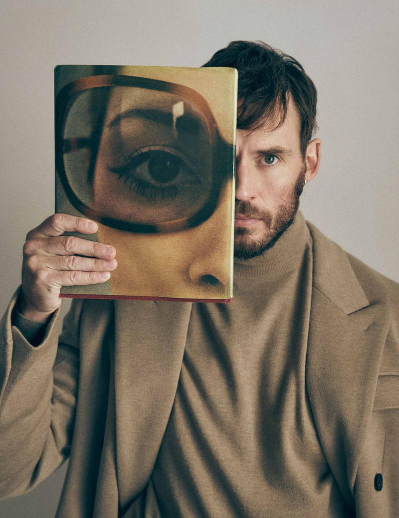Portrait of a man holding a book with an illustration of a woman's face. The book covers half of his face, creating a unique composition.
