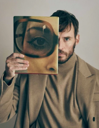 Portrait of a man holding a book with an illustration of a woman's face. The book covers half of his face, creating a unique composition.