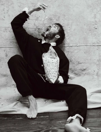 Black and white portrait of a bearded man sitting while holding a bag of popcorn and throwing some into his open mouth.